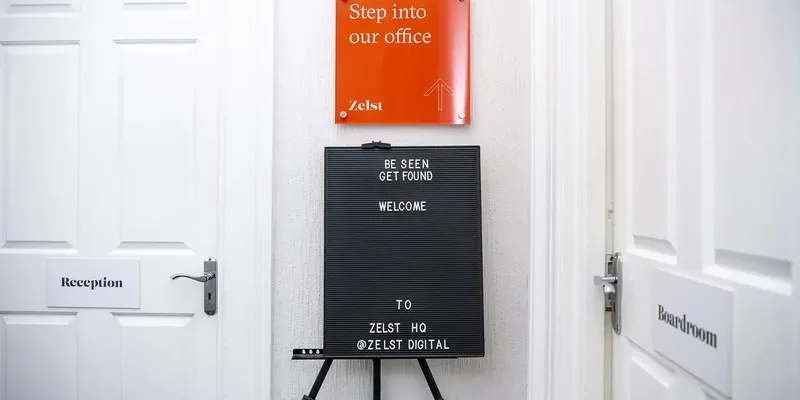 Two signs placed in the center of two white doors, saying step into our office and be seen get found, welcome to zelst hq